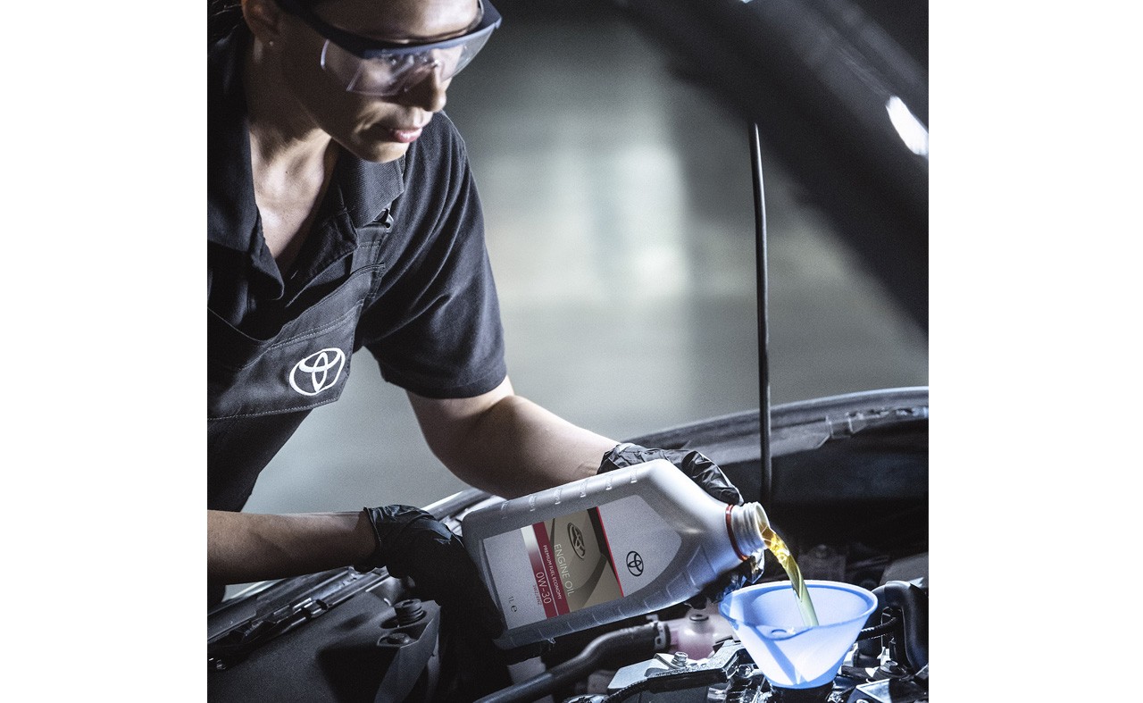 Female mechanic pouring toyota engine oil into a car