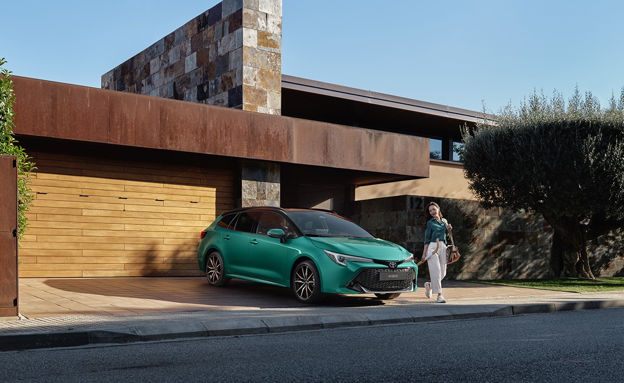 Woman walking out of a modern house, and around a parked green Toyota Corolla