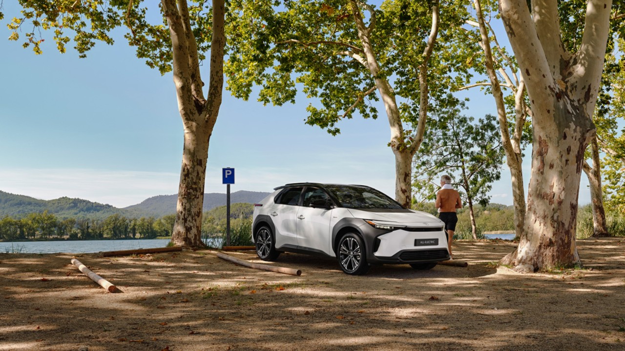 White bz4X parked overlooking a natural landscape. Man stood next to the car admiring the view 