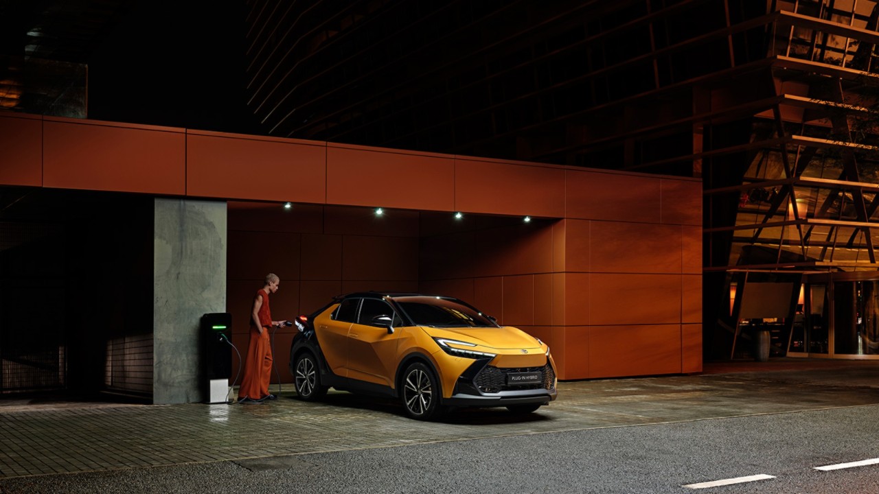 Man wearing fashionable orange outift stood by orange C-HR, outside of a dimly lit parking garage.