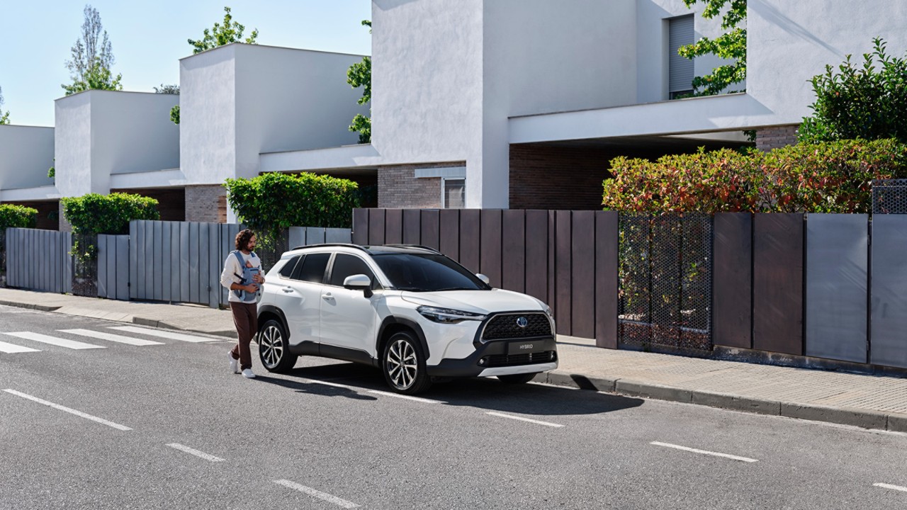 Man with a child, leaving their modern house, walking towards their parked white Corolla Cross,