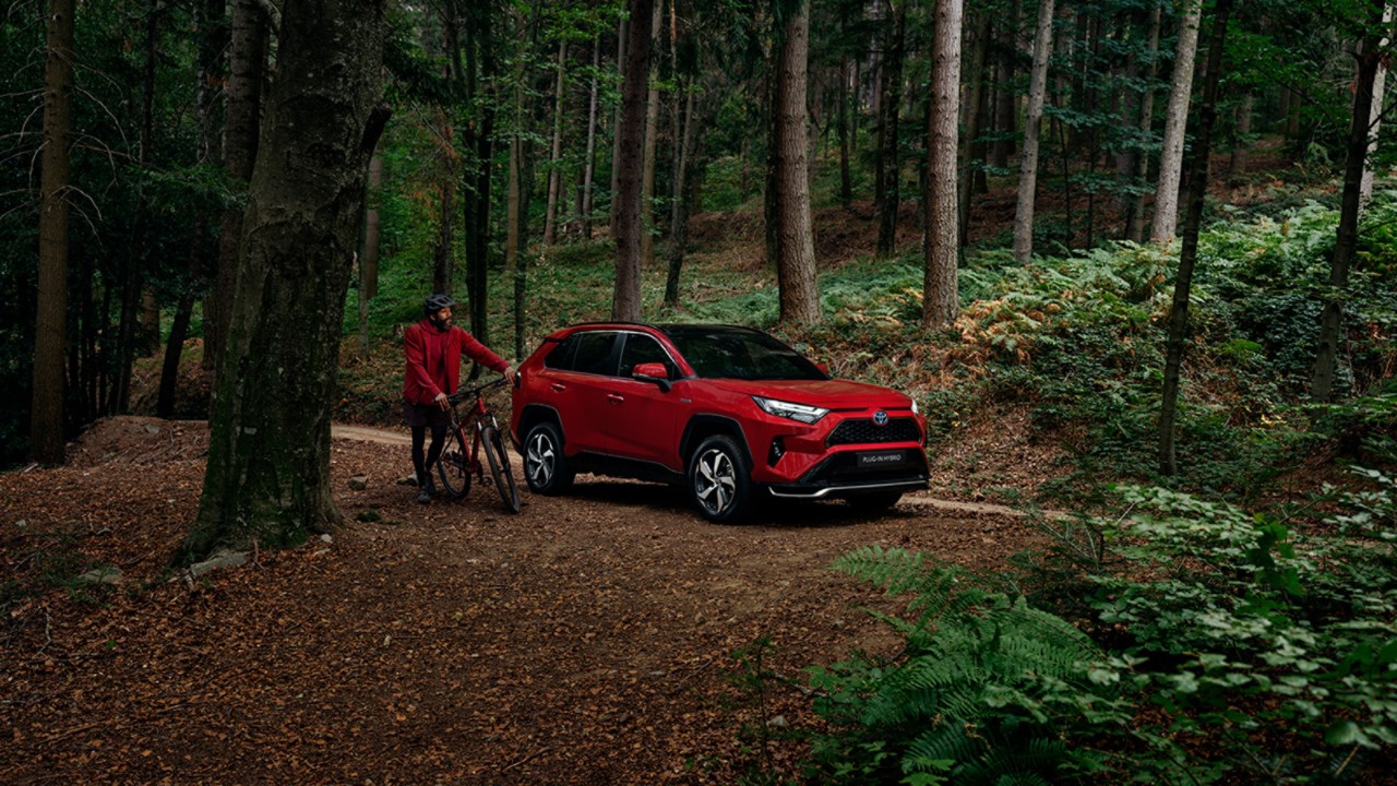 Man in red jacket, stood with a bike next to a red RAV4, in a forest