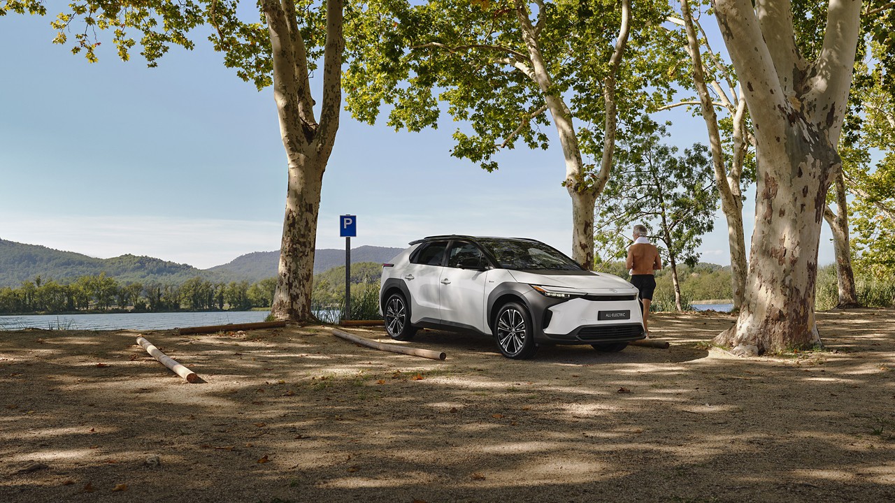 White bz4X parked overlooking a natural landscape. Man stood next to the car admiring the view 